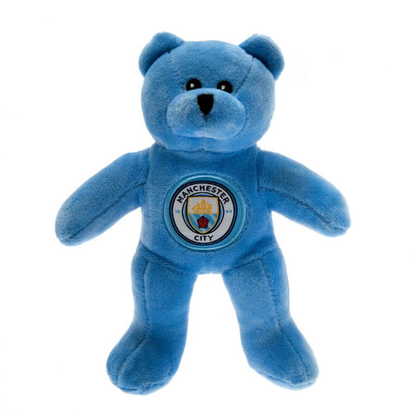 Blå bamse med "MANCHESTER CITY" logo på brystet, blød og krammevenlig, officiel merchandise.