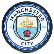 Rundt LED-skilt med Manchester Citys logo, skib, rød rose og årstal 1894 i blå og guld farver.