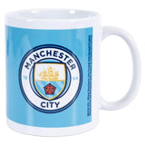 Krus med Manchester City logo, skib, rød rose og tallet 1894 på lyseblå baggrund.